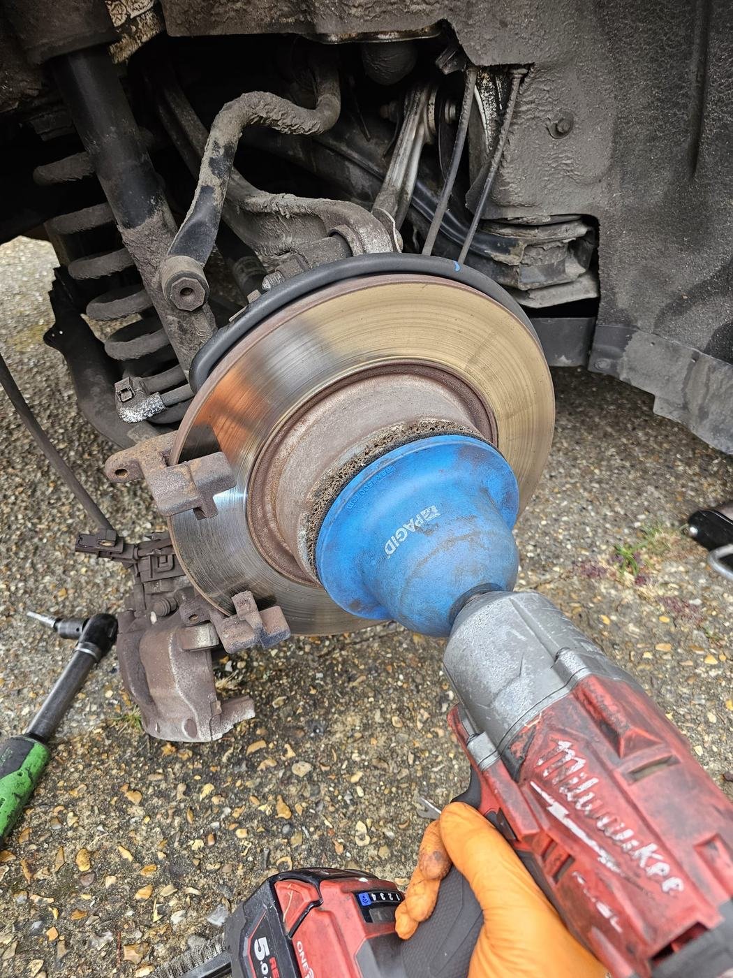 A brake disc and caliper being worked on with a cordless impact tool