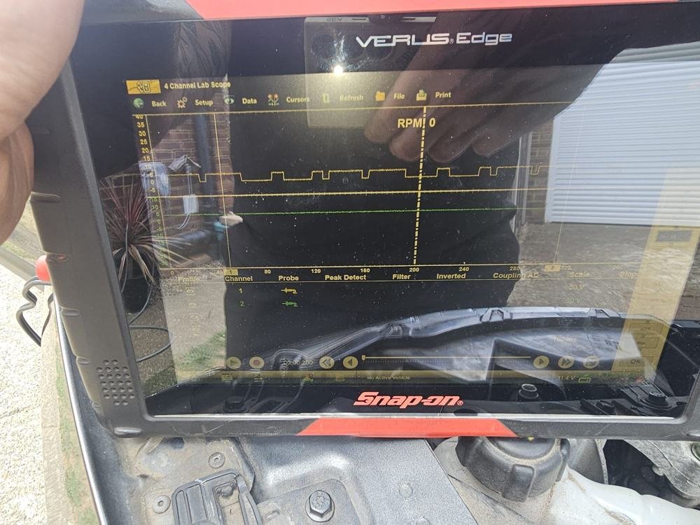 A diagnostic tablet showing a live signal trace beside a car