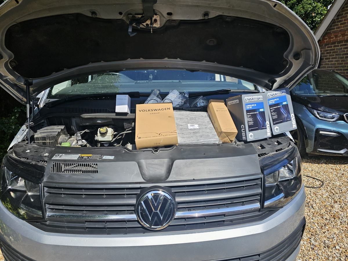 Filters and engine oil boxes lined up on a van with its bonnet open, ready for a service