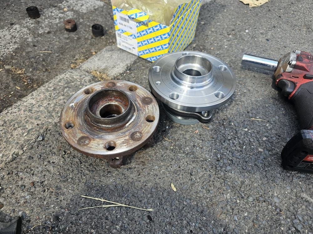 Two wheel hub units laid out on the ground beside a cordless tool